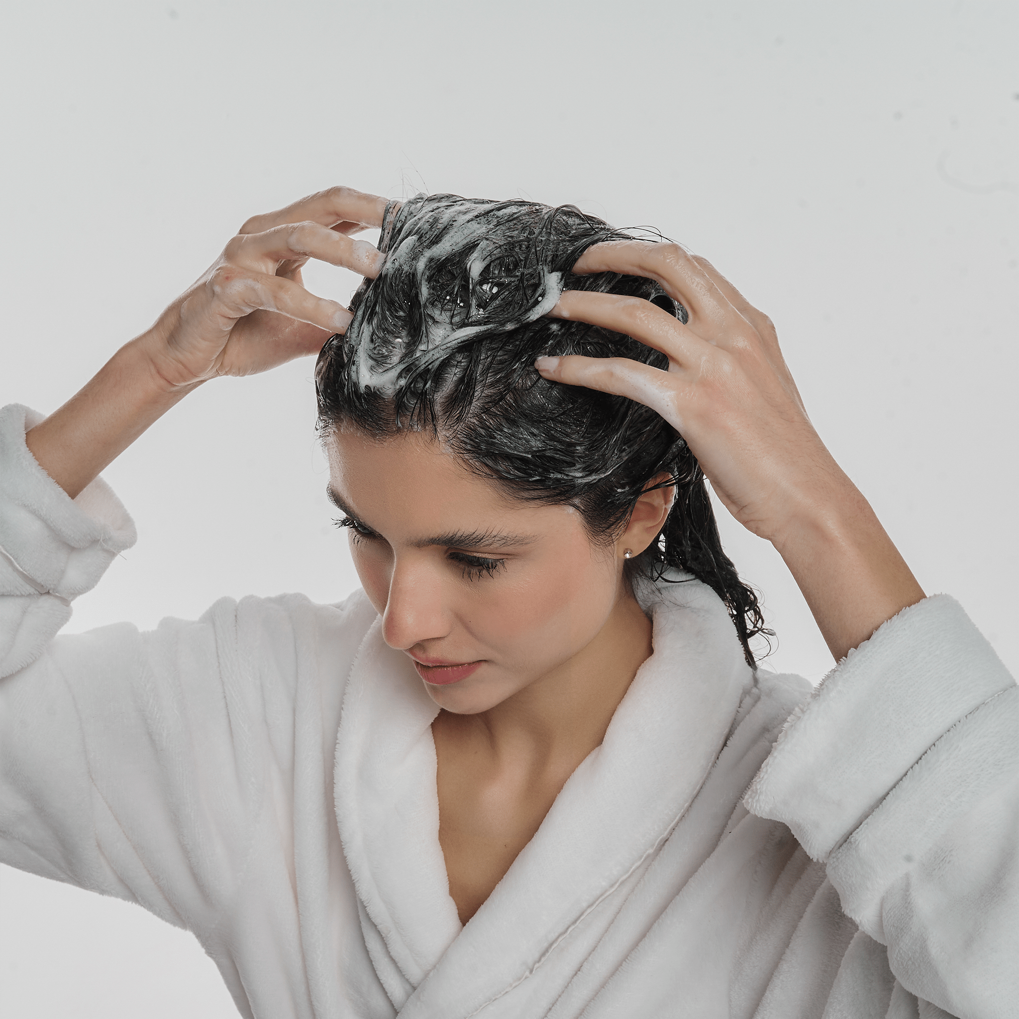 Mulher morena com o cabelo espumado com o shampoo anticaspa.