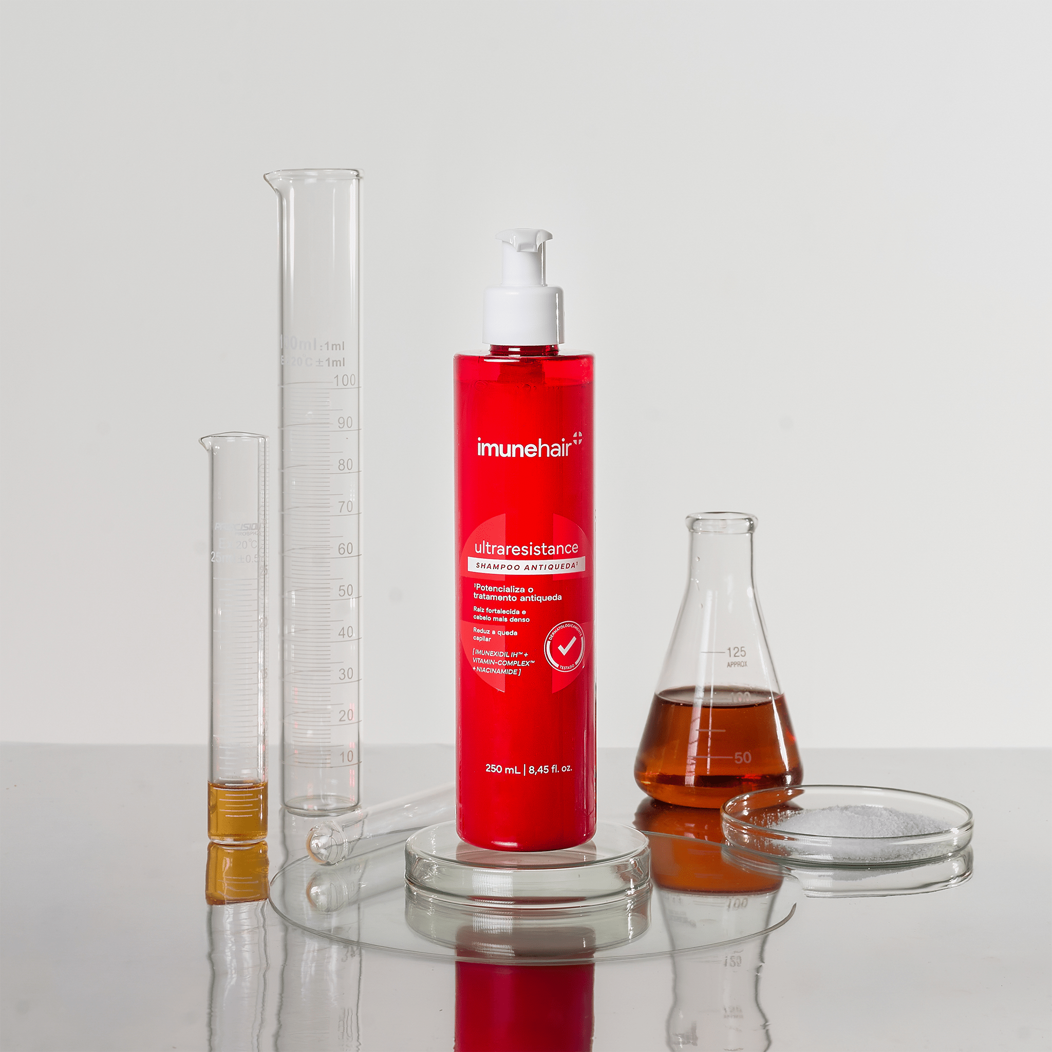 Embalagem vermelha do Shampoo Antiqueda Ultraresistance com 250ml. Plaquetas e béquer com os ativos presentes na formulação do shampoo antiqueda.