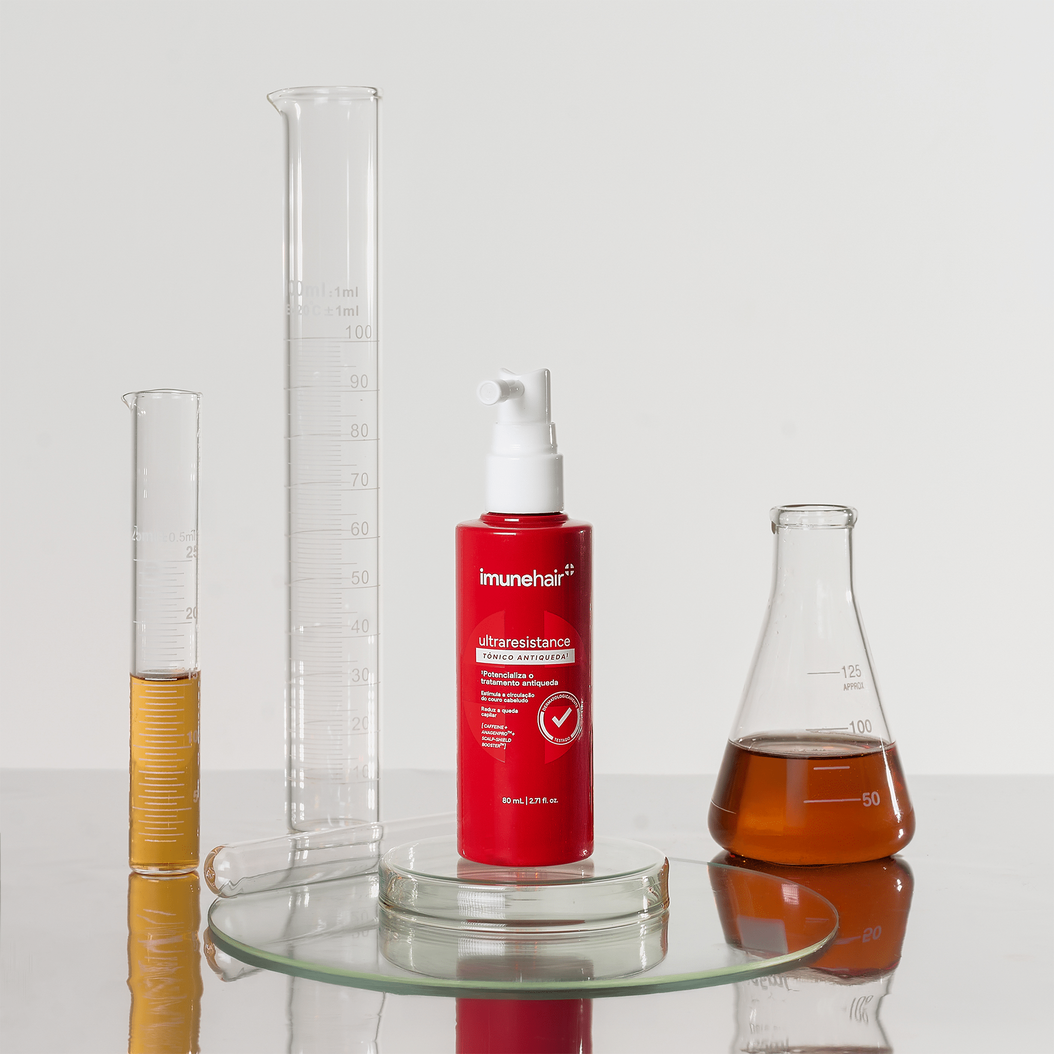 Embalagem vermelha do Tônico Antiqueda Ultraresistance de 80ml. Béquer e provetas com os ativos presentes na formulação do tônico antiqueda.